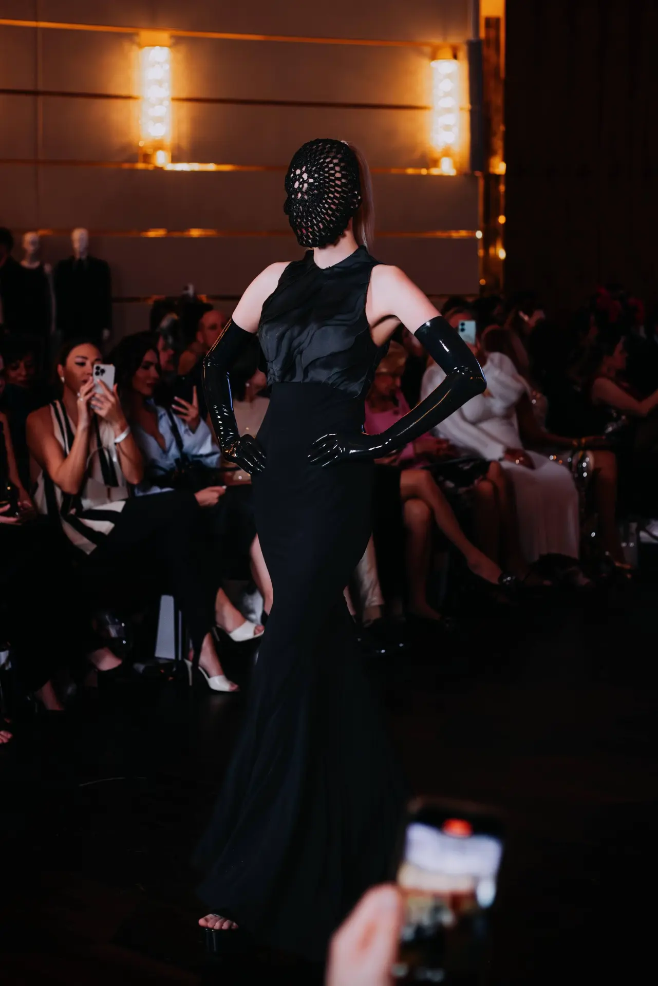 Model in a black couture gown, latex gloves and lace mask on the Couture Fashion Night runway