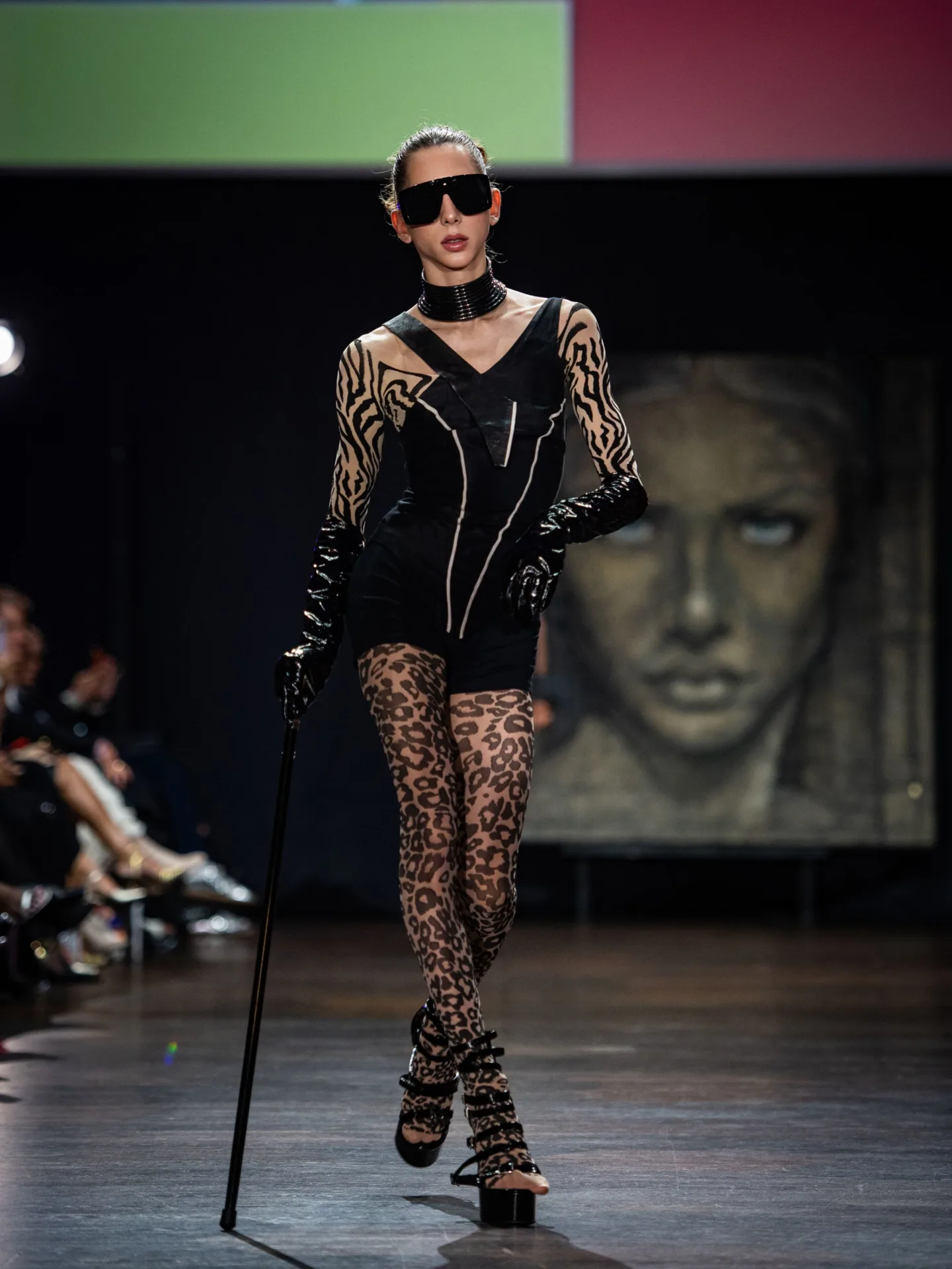 Model in a black jumpsuit with leopard-print tights, glossy gloves and sunglasses on the CFN 4.0 runway