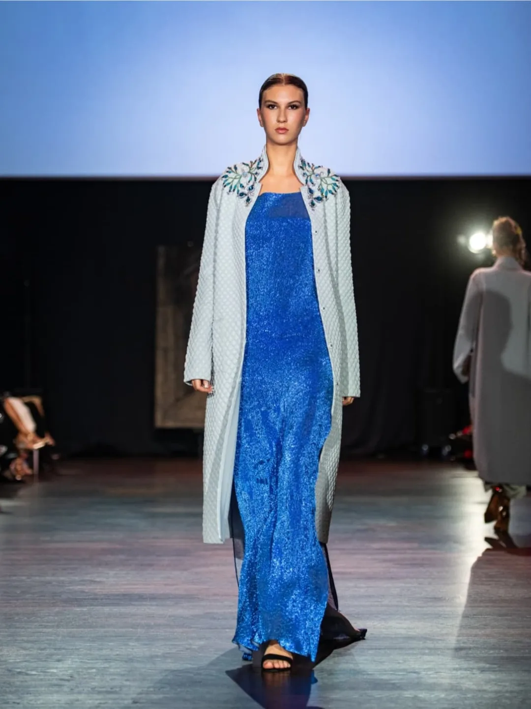 Model in a cobalt blue lace gown with a pale coat and an embellished collar by DOBRZANSKA