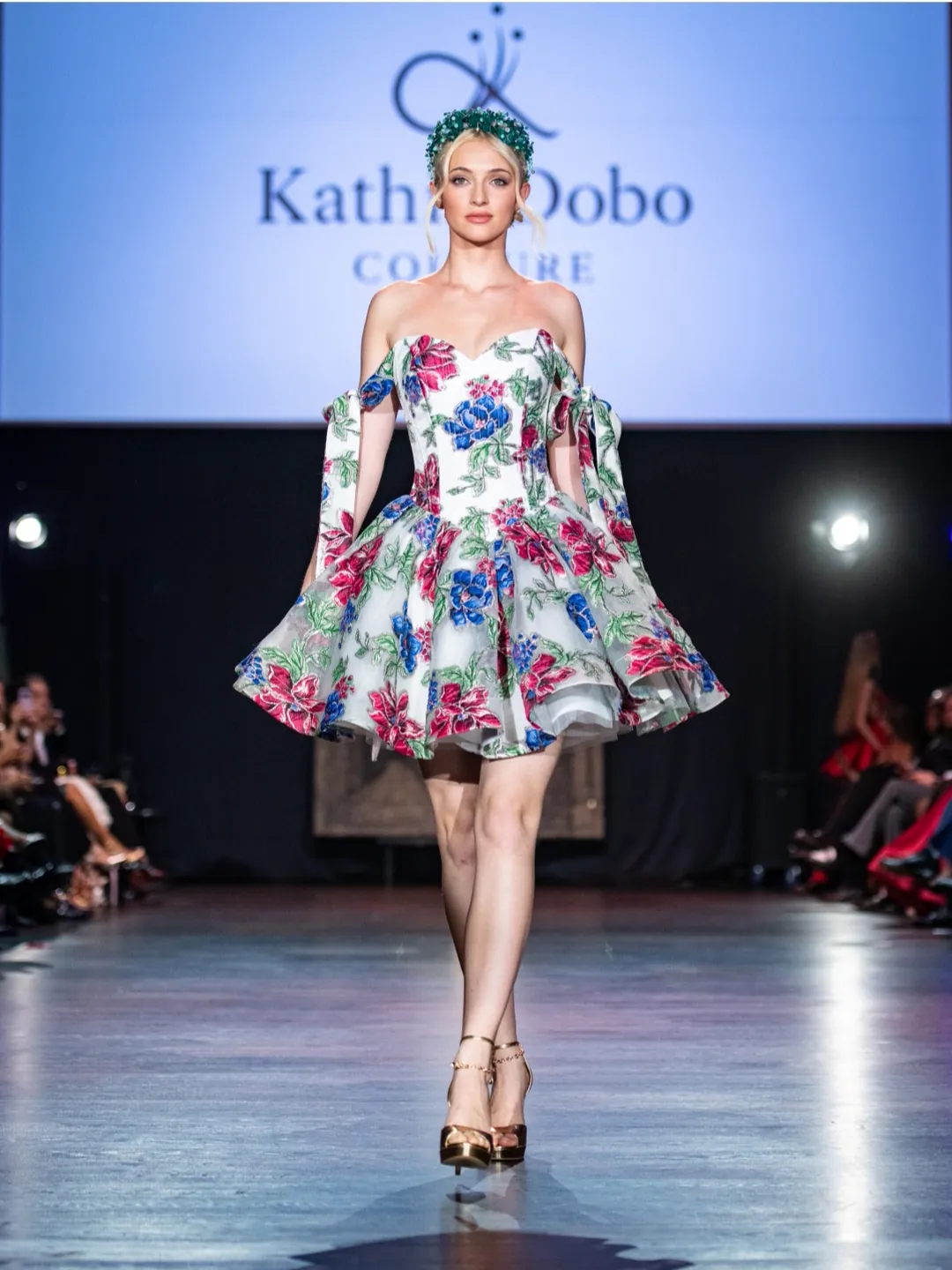 Model in a white embroidered mini dress with magenta and blue florals and gold platforms by Kathia Dobó